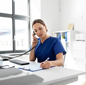 Image of nurse in blue scrubs on the phone conducting a telehealth appointment