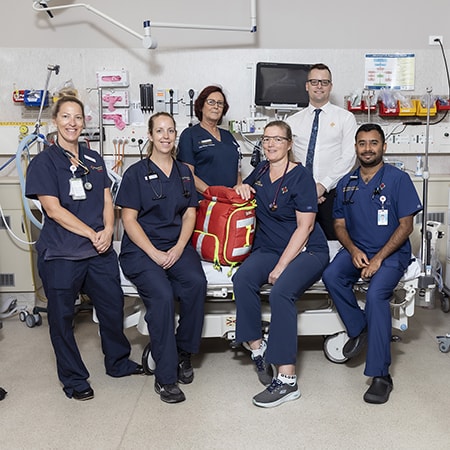Caregievrs dressed in dark blue scrubs surround a bed inside the Emergency Department