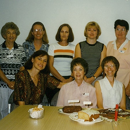 Eight caregivers from the Palliative Care Unit in Thomas Furlong Ward behind a table containing baked goods
