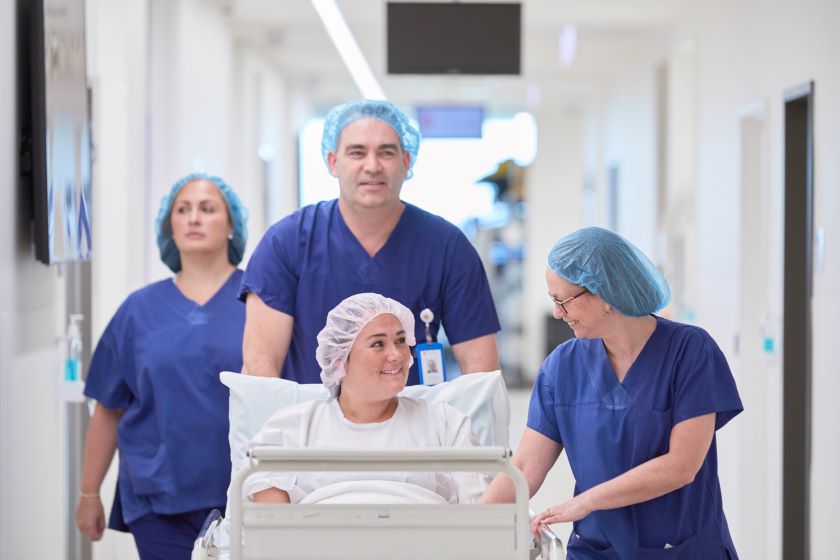 Patient in surgical gown wheeled into theatre by three caregivers