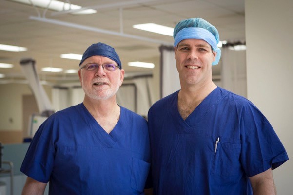 Dr Bruce Thyer with son Dr Matt Thyer in operating theatre scrubs and hats. 
