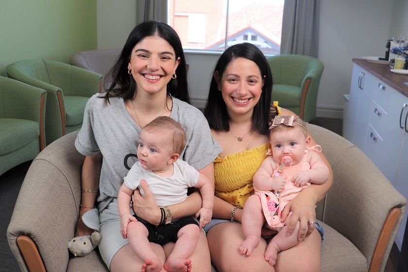 Two mothers sitting on a couch with their infants in their laps