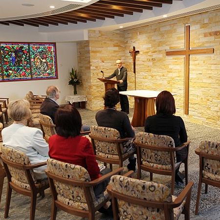 Interior of Chapel in 1994 with people seated in chairs facing man speaking at lectern