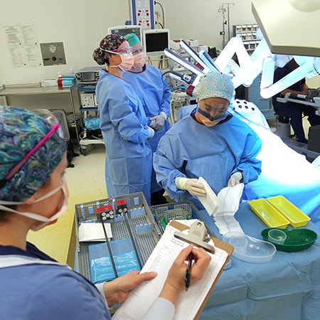 Four caregivers standing and dressed in surgical attire in a theatre performing da Vinci robotic surgery