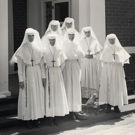 Black and white photograph of seven Sisters of St John of God wearing white habits standing outside the Rivervale hospital circa 1950