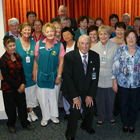 A group of volunteers and caregivers wearing uniforms and badges stand together and smile at the camera