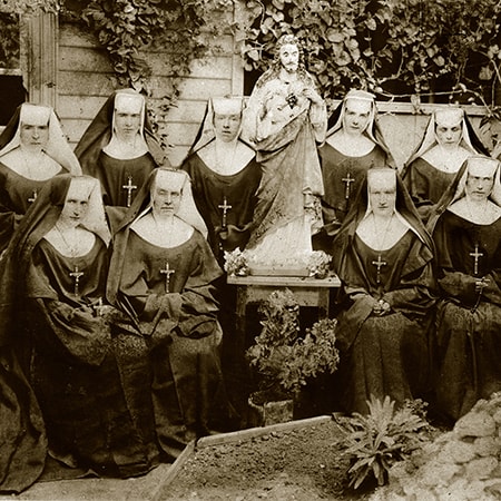 Black and white photograph of the pioneer Sisters of St John of God sitting beside a statue, taken in 1897